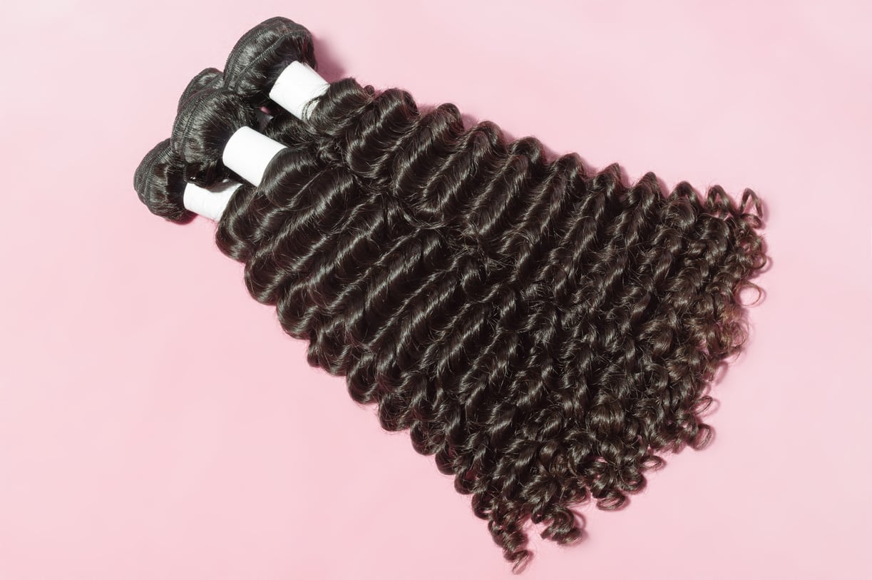 Deep curly black human hair weaves extensions bundles upon pink background